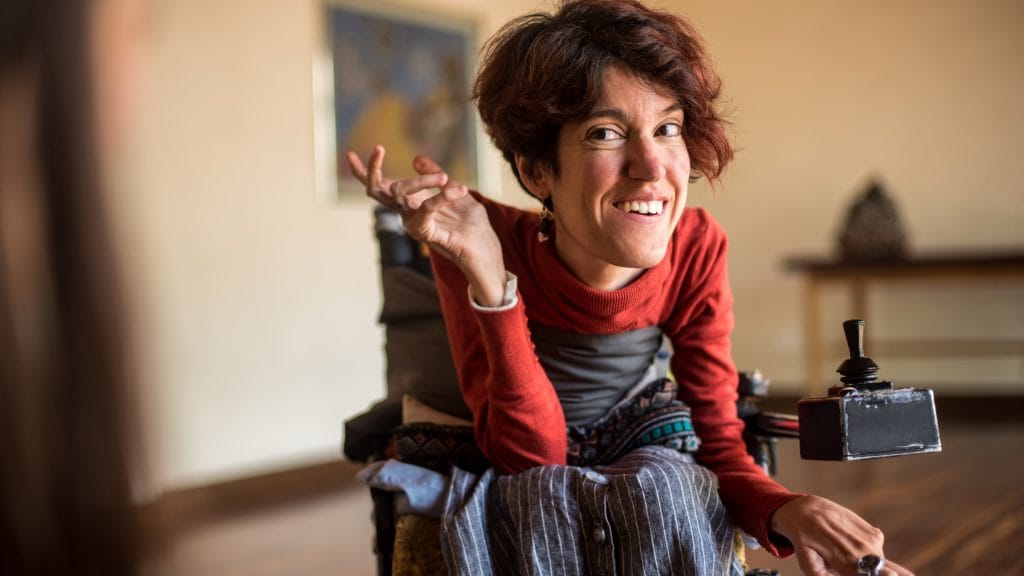 Woman in electric wheelchair, leaning forward and smiling.